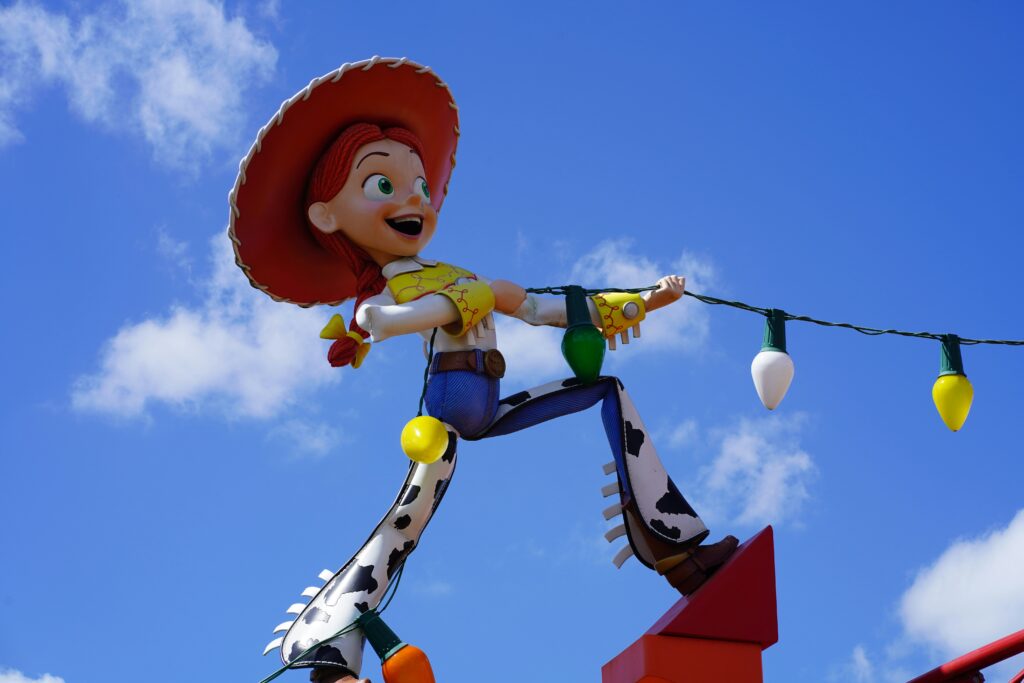 Toy story character in a cow girl outfit working away holding up some coloured lights against a blue sky with white tufts of cloud.